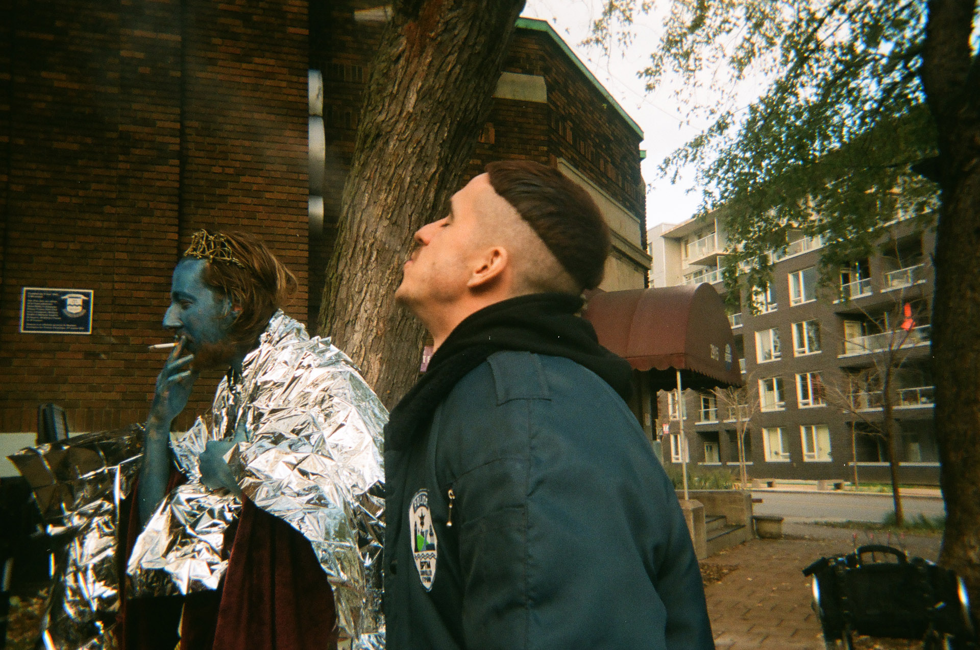 actor Emile Schneider dressed as cop and actor playing cult guru all covered in blue makeup keeping warm with safety blanket both smoking cigarettes in behind the scenes of TV series La Loi C'est La Loi filmed by Les Gamins for TV5 Unis
