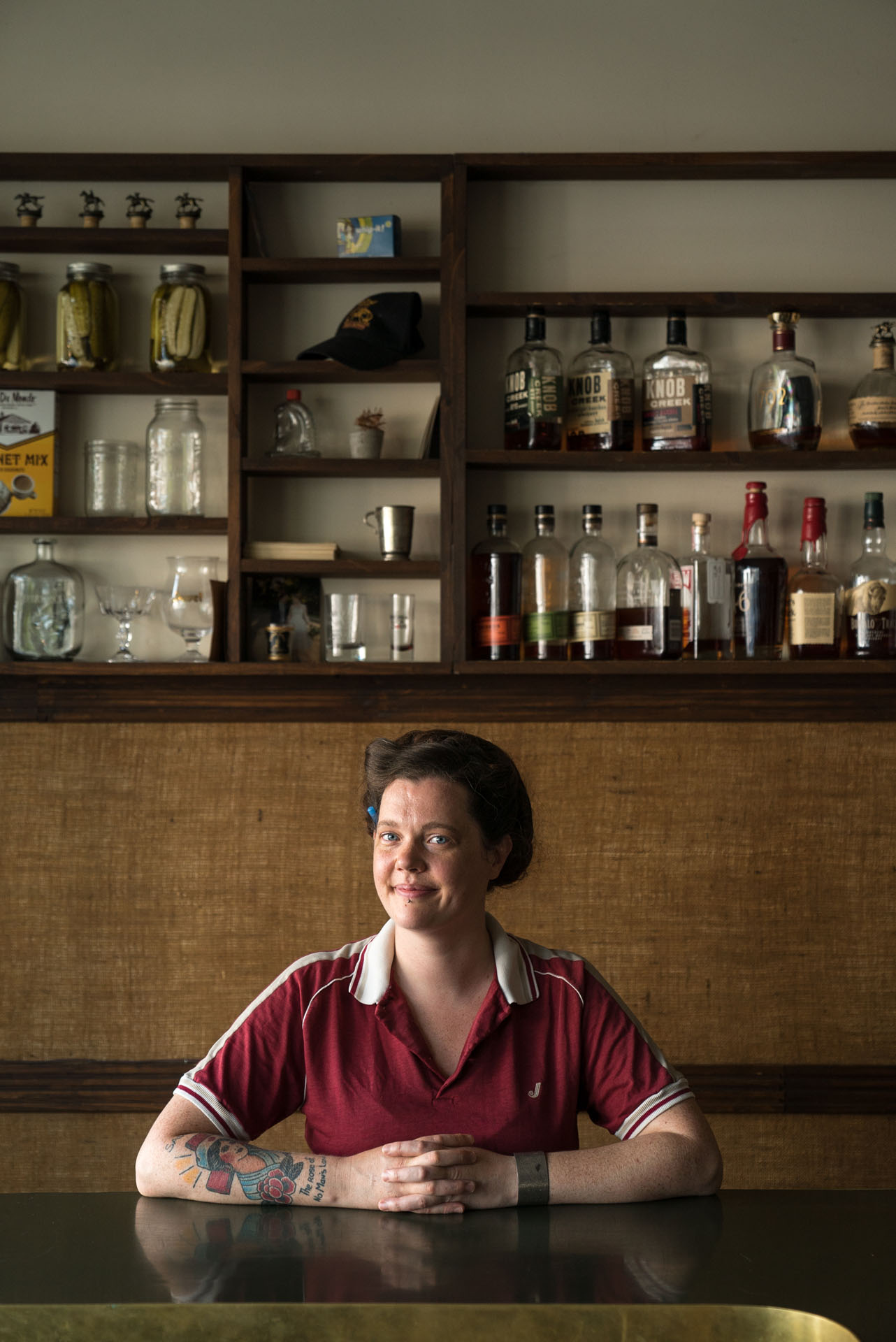 female bar owner sitting at table in front of wall with bottles by Bruno Florin for mile ex mille vie