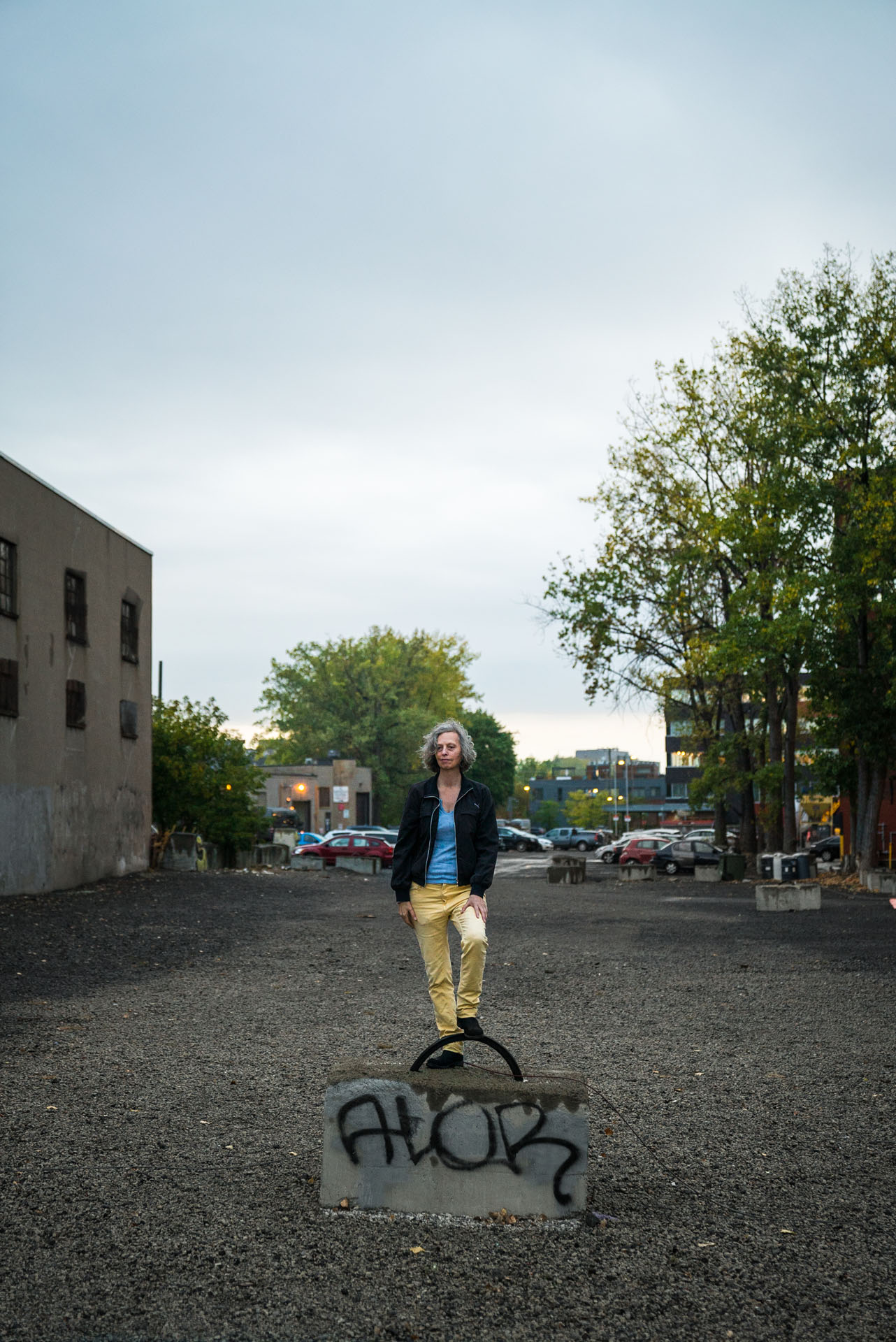 grey haired woman posing on concrete block in empty parking lot by Bruno Florin for mile ex mille vie