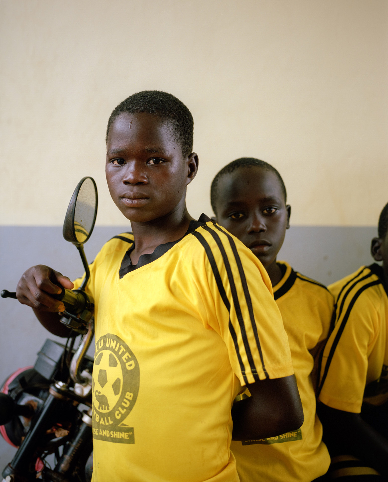 close up of young black boys on scooter looking at camera by Alexi Hobbs in Uganda for Football for good with Sportsnet