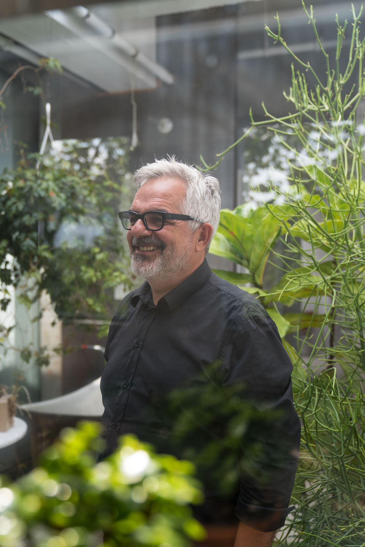 white haired man wearing glasses and black shirt posing inside greenhouse among plants by Bruno Florin for mile ex mille vie