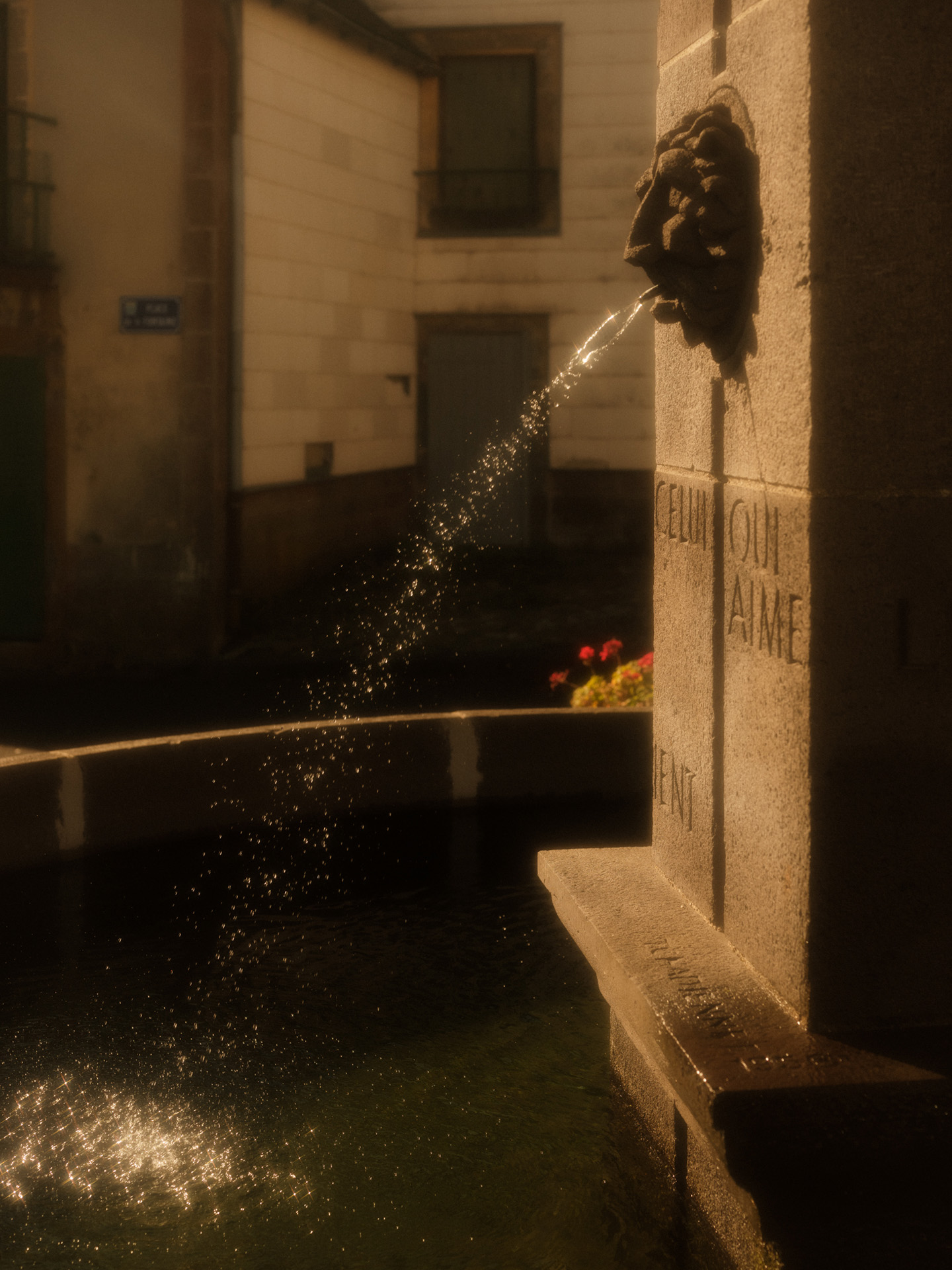 fountain with lionhead spitting water in the sun by Alexi Hobbs in Auvergne for Reflets de France