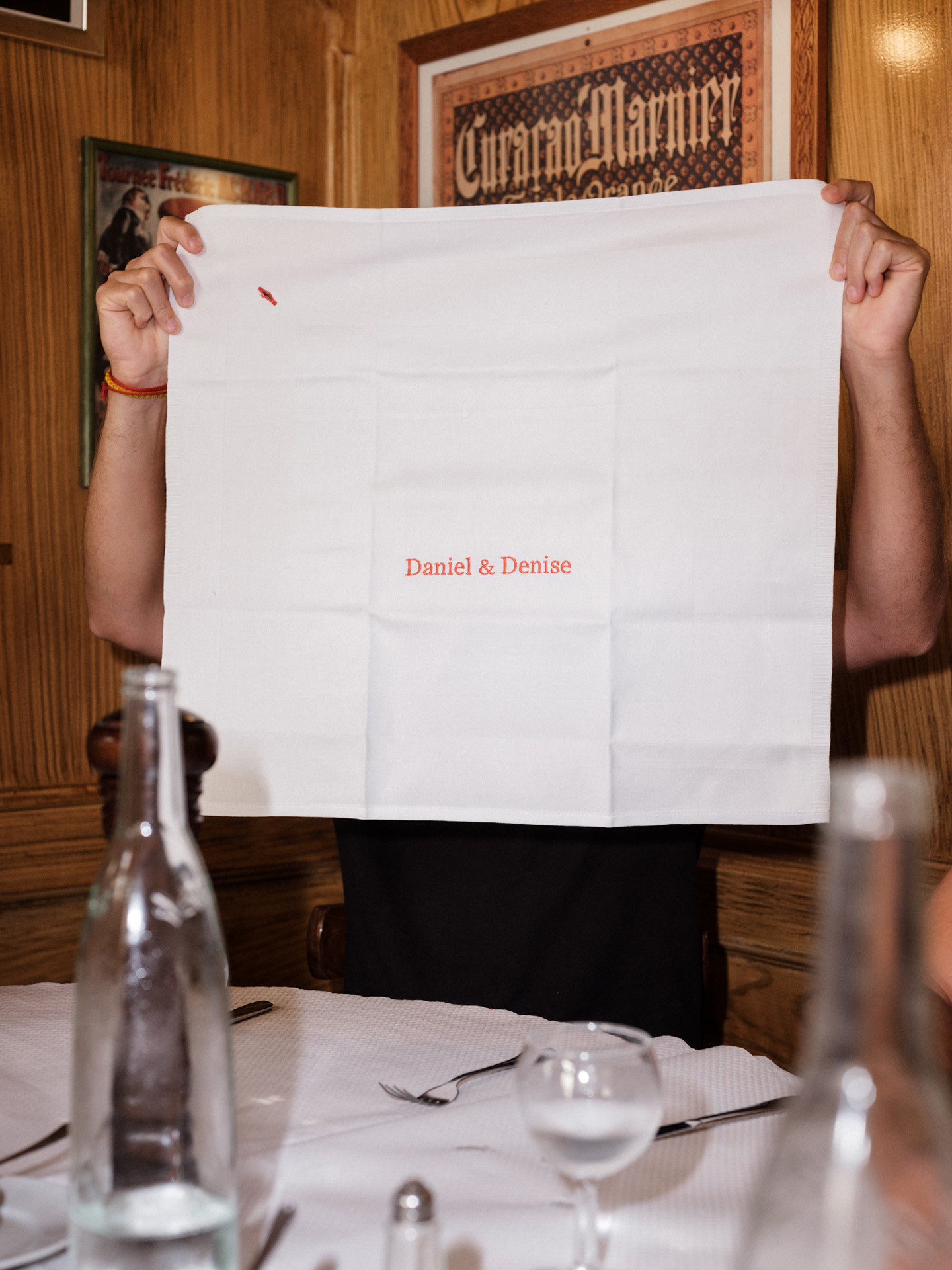 man holding up a white fabric napkin with 'Daniel & Denise' embroidered in red by Alexi Hobbs in Auvergne for Reflets de France
