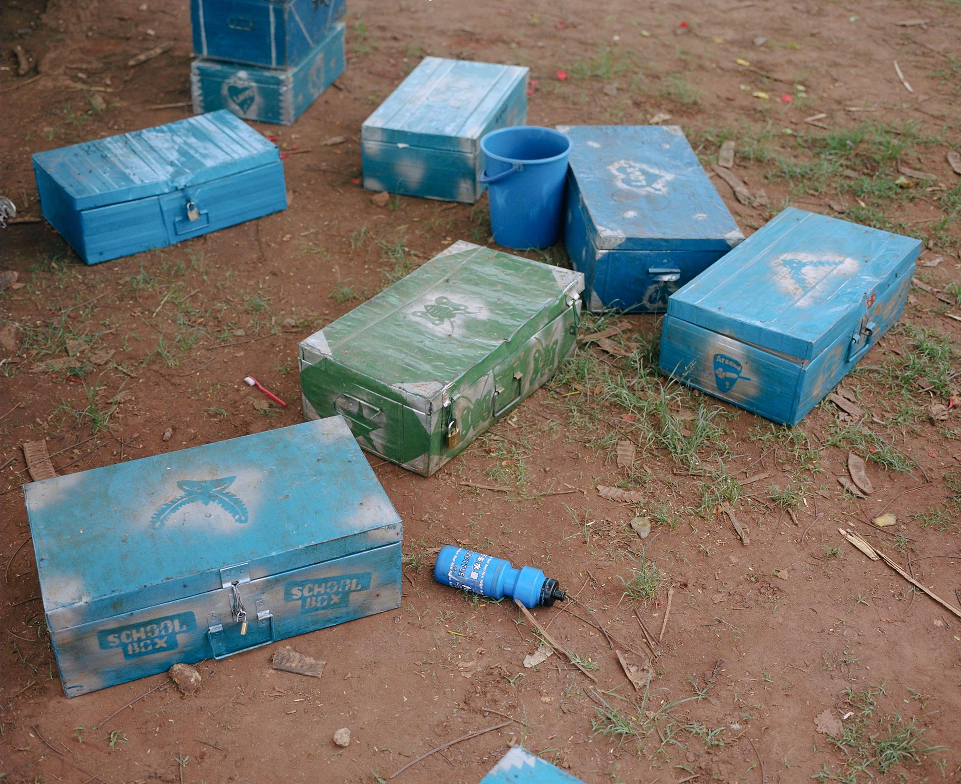 blue metal chests on the ground decorated and labeled school boxes with blue water bottle around by Alexi Hobbs in Uganda for Football for Good with Sportsnet