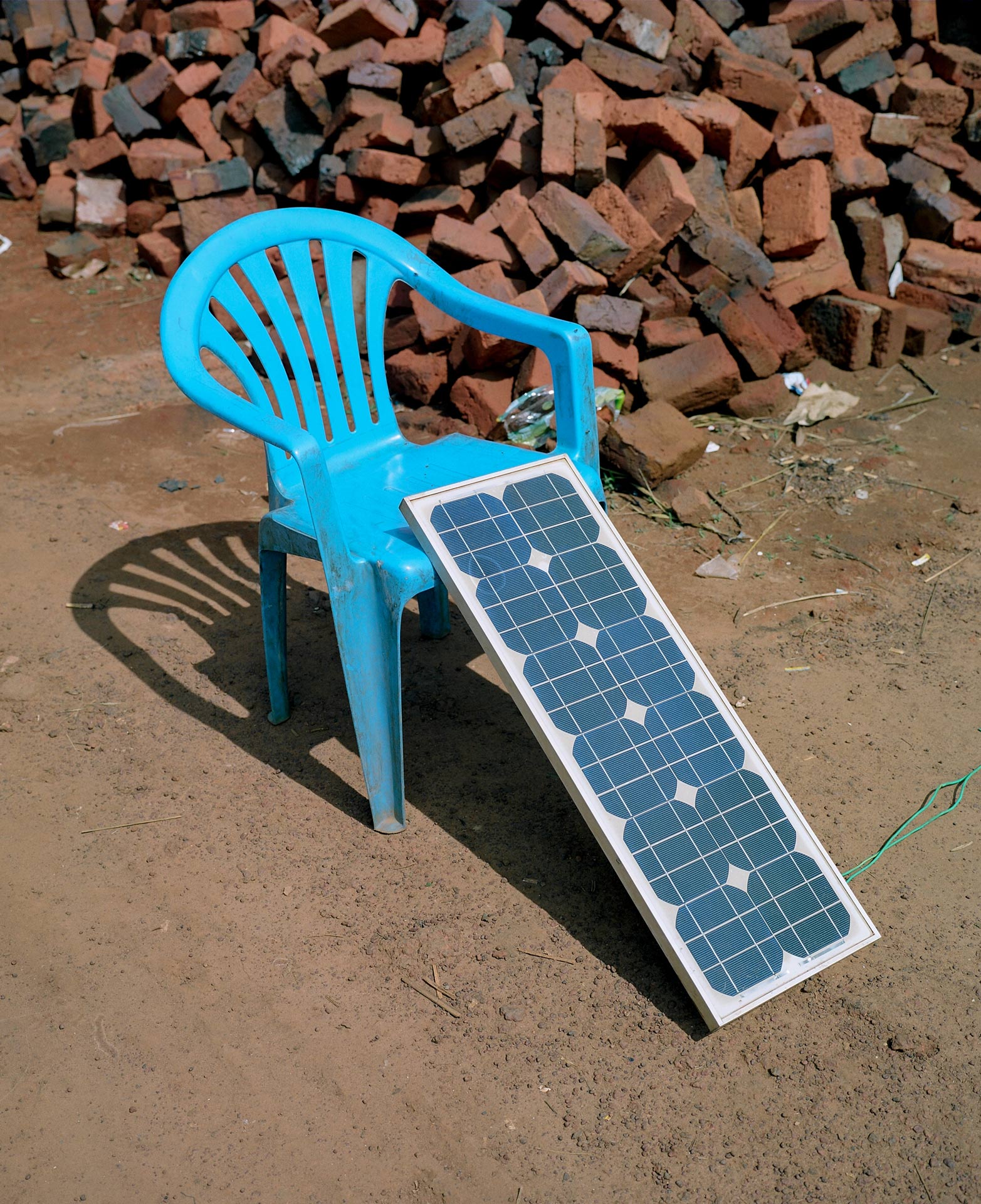 blue plastic chair supporting a transportable solar panel while its recharging by Alexi Hobbs in Uganda for Football for Good with Sportsnet