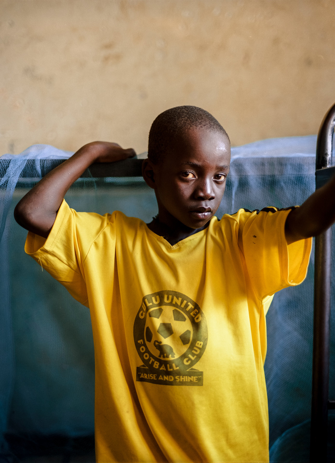 young black boy looking at camera wearing yellow soccer jersey by Alexi Hobbs in Uganda for Football for Good with Sportsnet