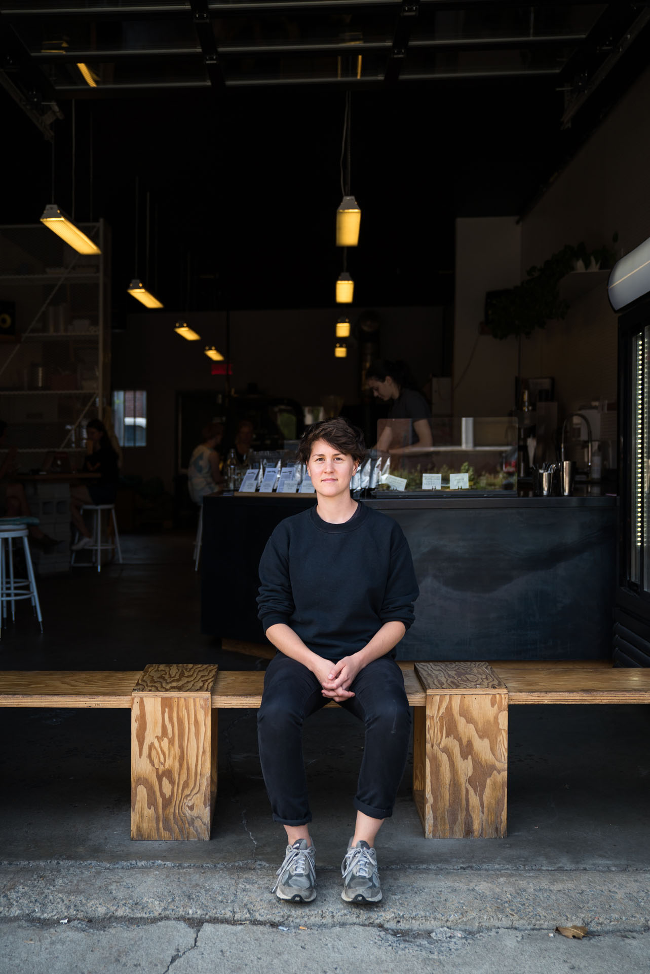 young woman sitting on wood bench before a coffee shop by bruno florin for mile-ex mille vies