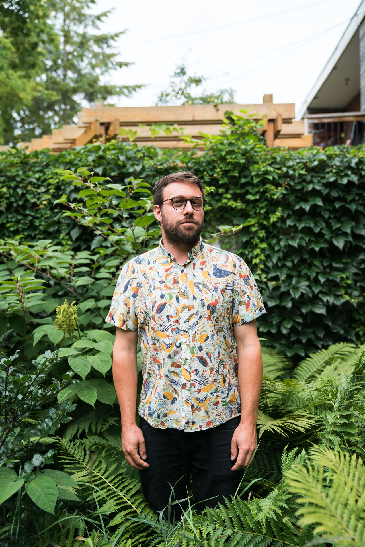 bearded man wearing shirt with colorful birds standing in middle of high plants by bruno florin for mile-ex mille vies
