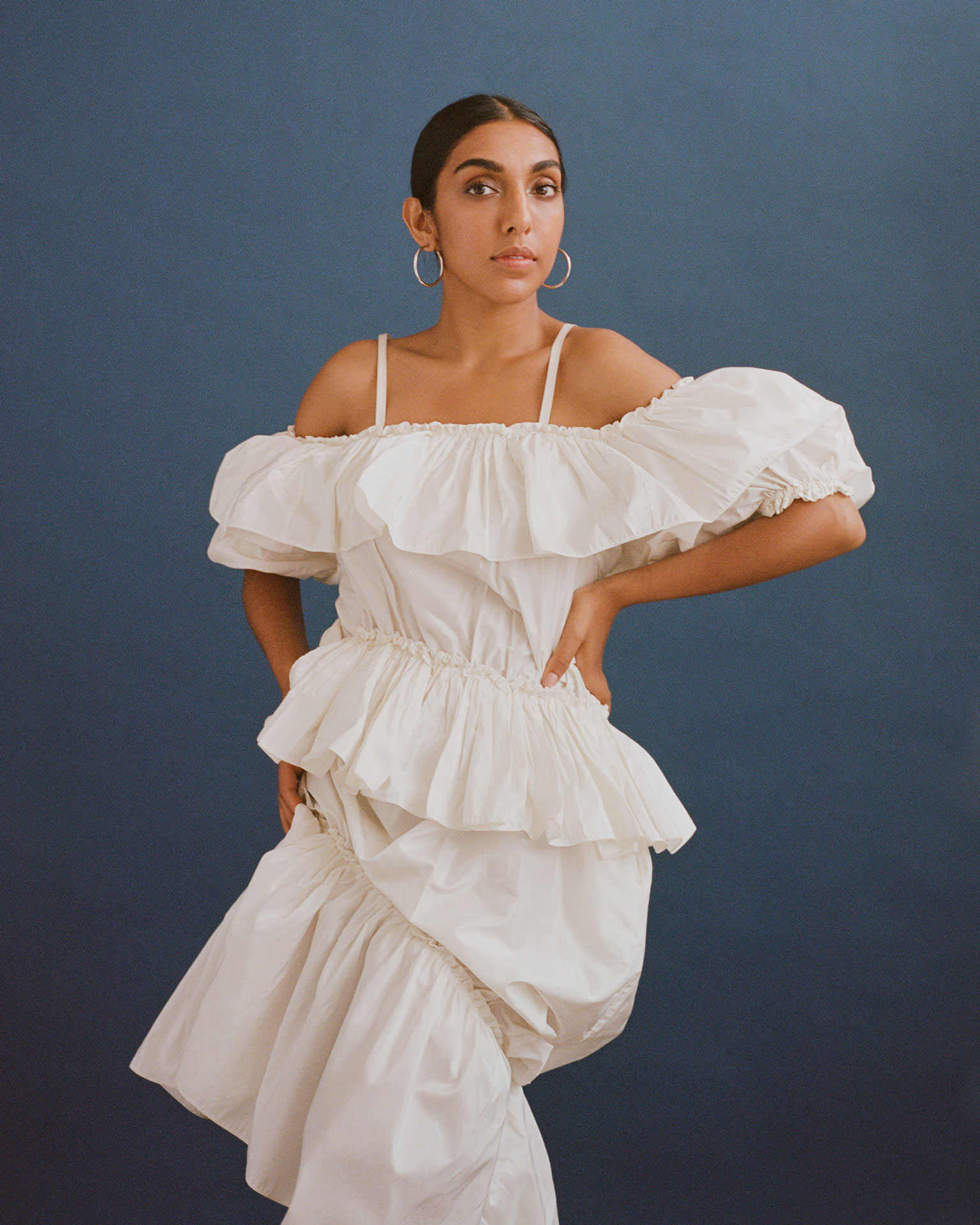 writer Rupi Kaur on blue background looking at camera wearing white dress by Oumayma B Tanfous for Vogue Espana
