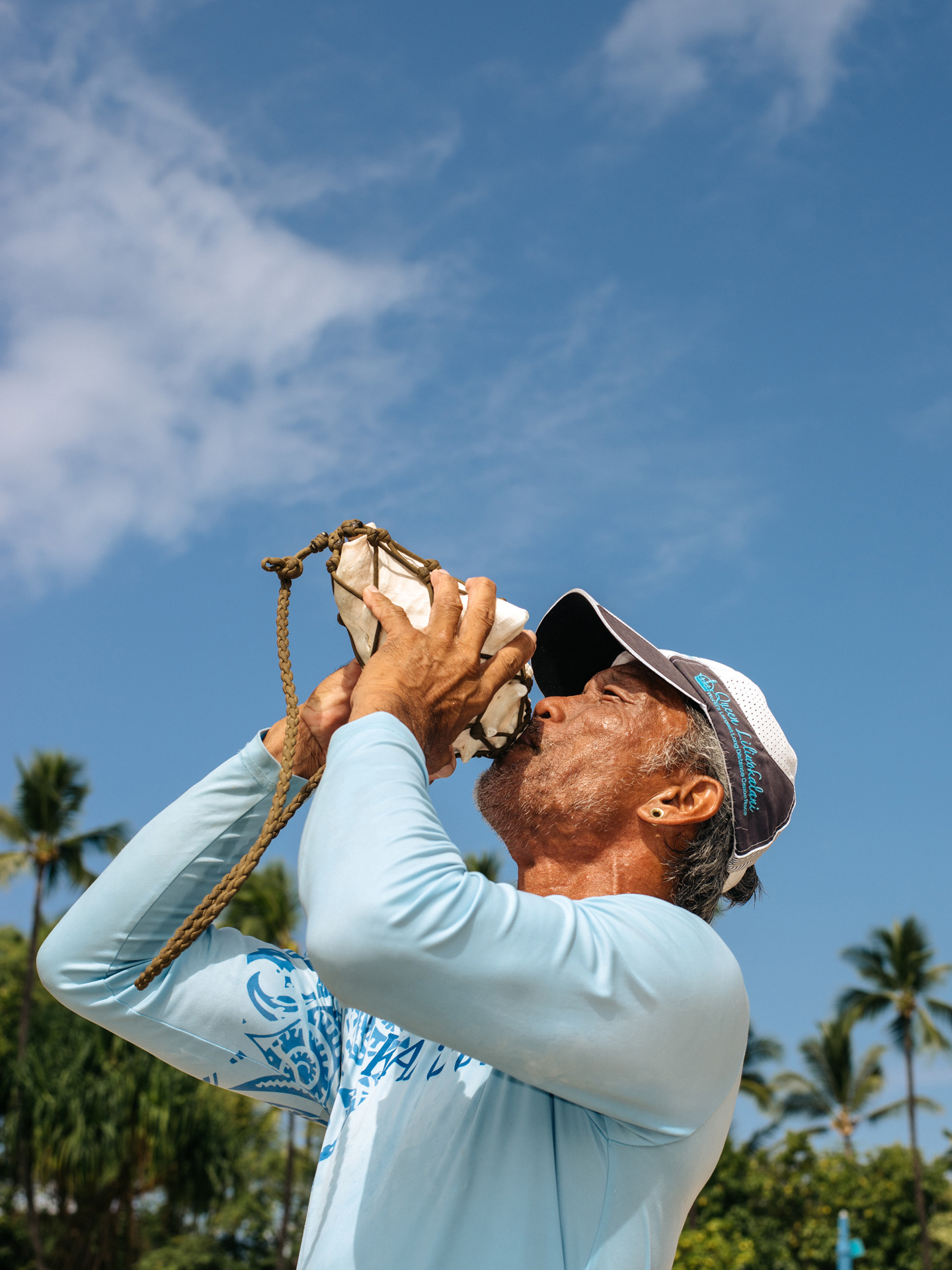 hawaiian male native blowing into big seashell conch by Alexi Hobbs in Hawaii for enRoute