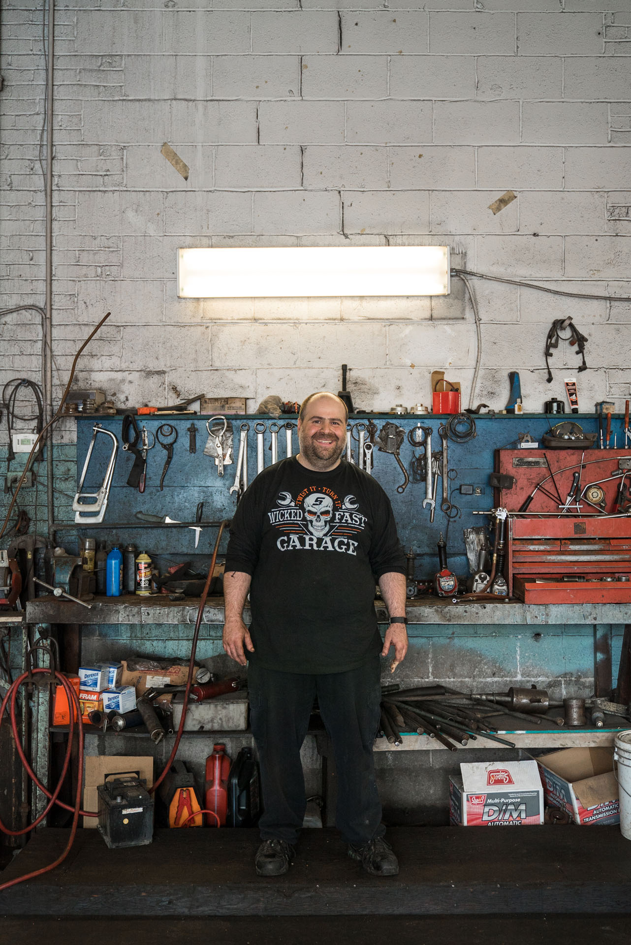 bald garage owner smiling posing in front of his work table with tools by Bruno Florin for Mile-Ex Milles vie