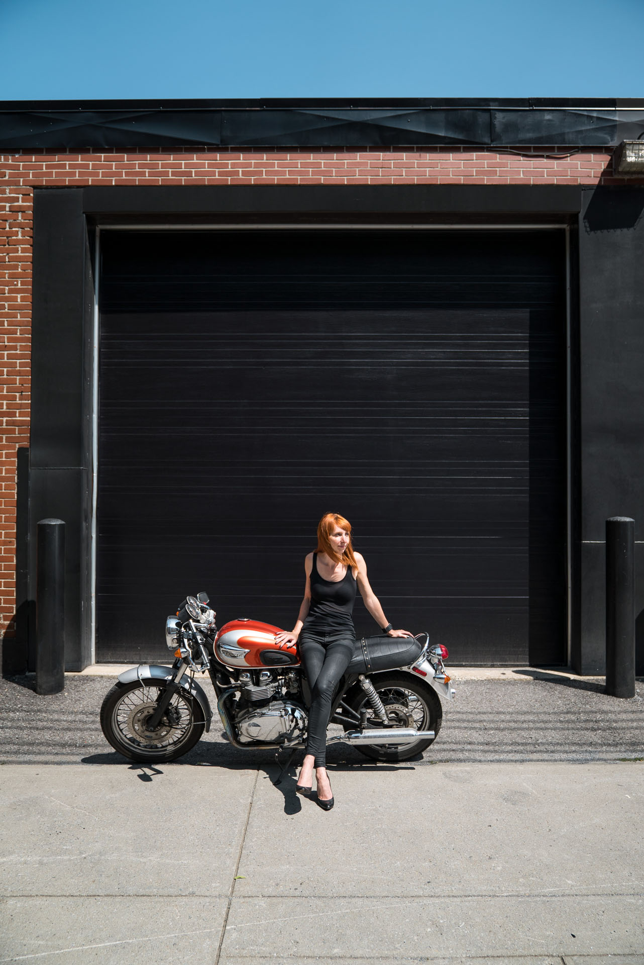 redheaded woman posing sitting on motorcycle in front of black garage by Bruno Florin for mile-ex mille vie