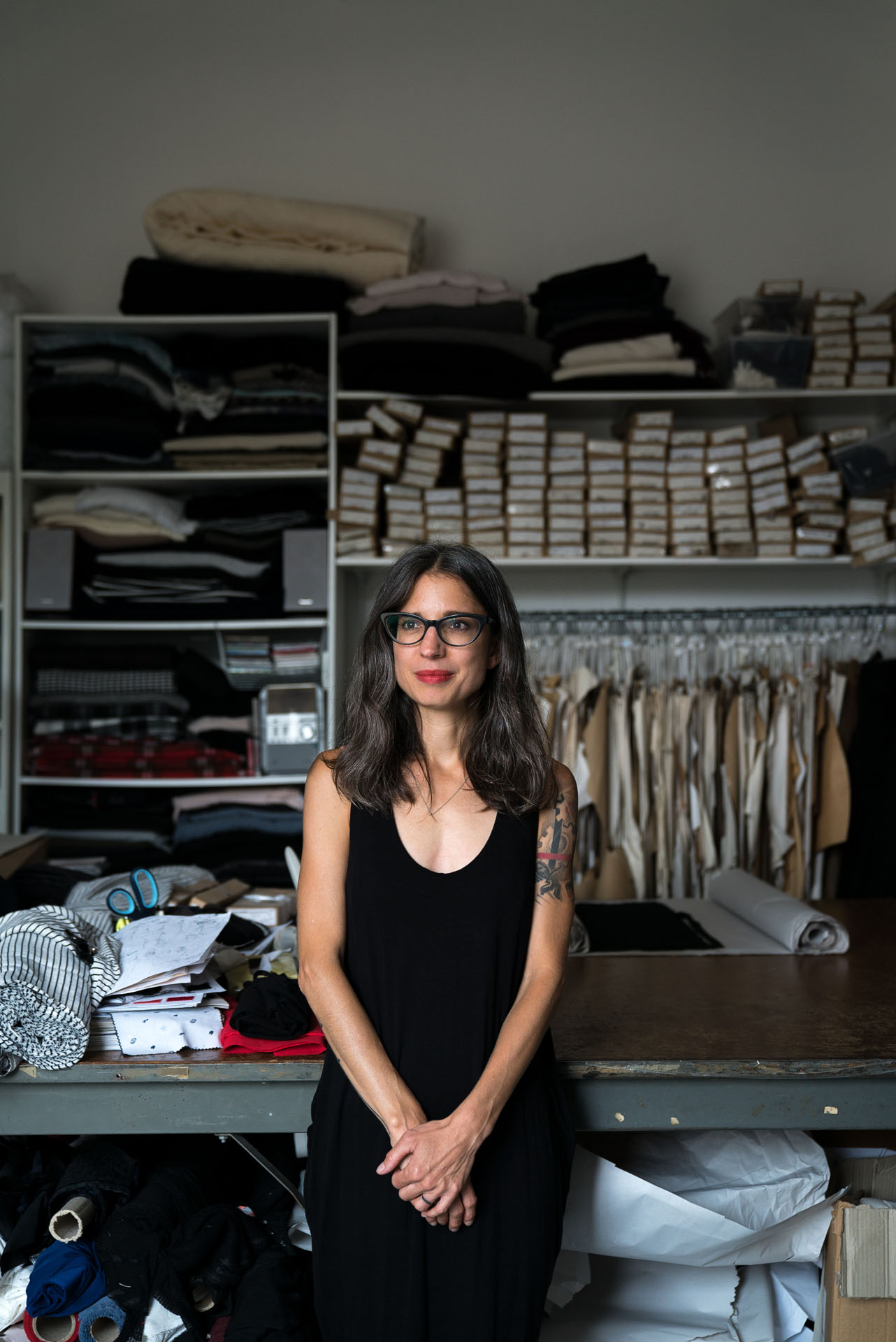 brown haired woman seamstress looking away posing in front of worktable with scissors and piles of fabric by Bruno Florin for mile-ex mille vie