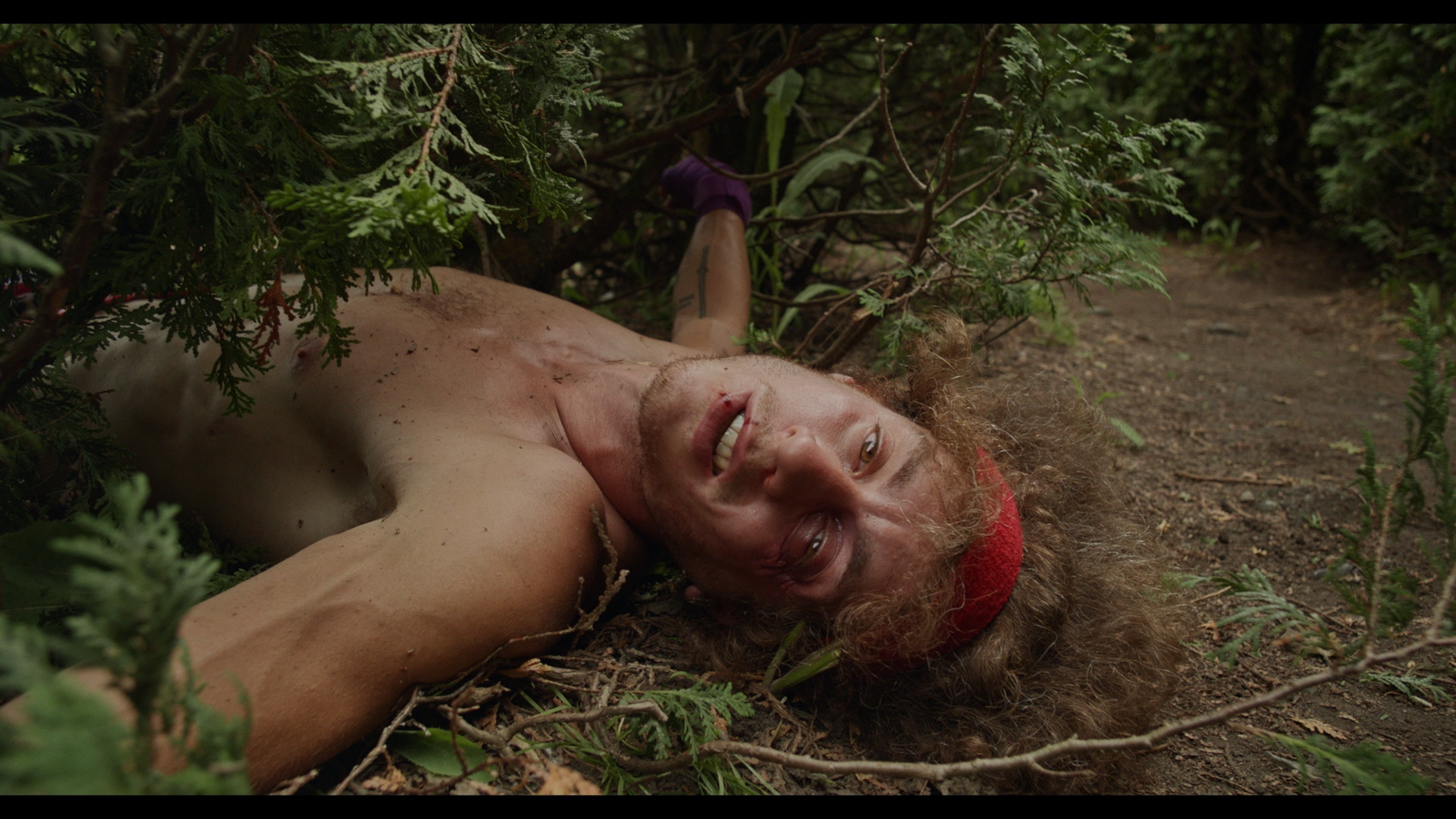 actor beaten up on the ground half his body under a bush looking directly at camera for Alaclair Ensemble hip hop collective music video Felix filmed by Les Gamins featuring Souldia