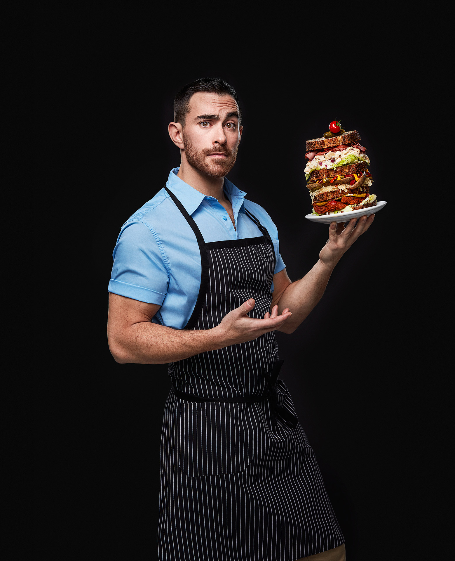 portrait of chief Alex Cohen holding a multi-layered sandwich almost falling over by Jocelyn Michel for the Cathcart