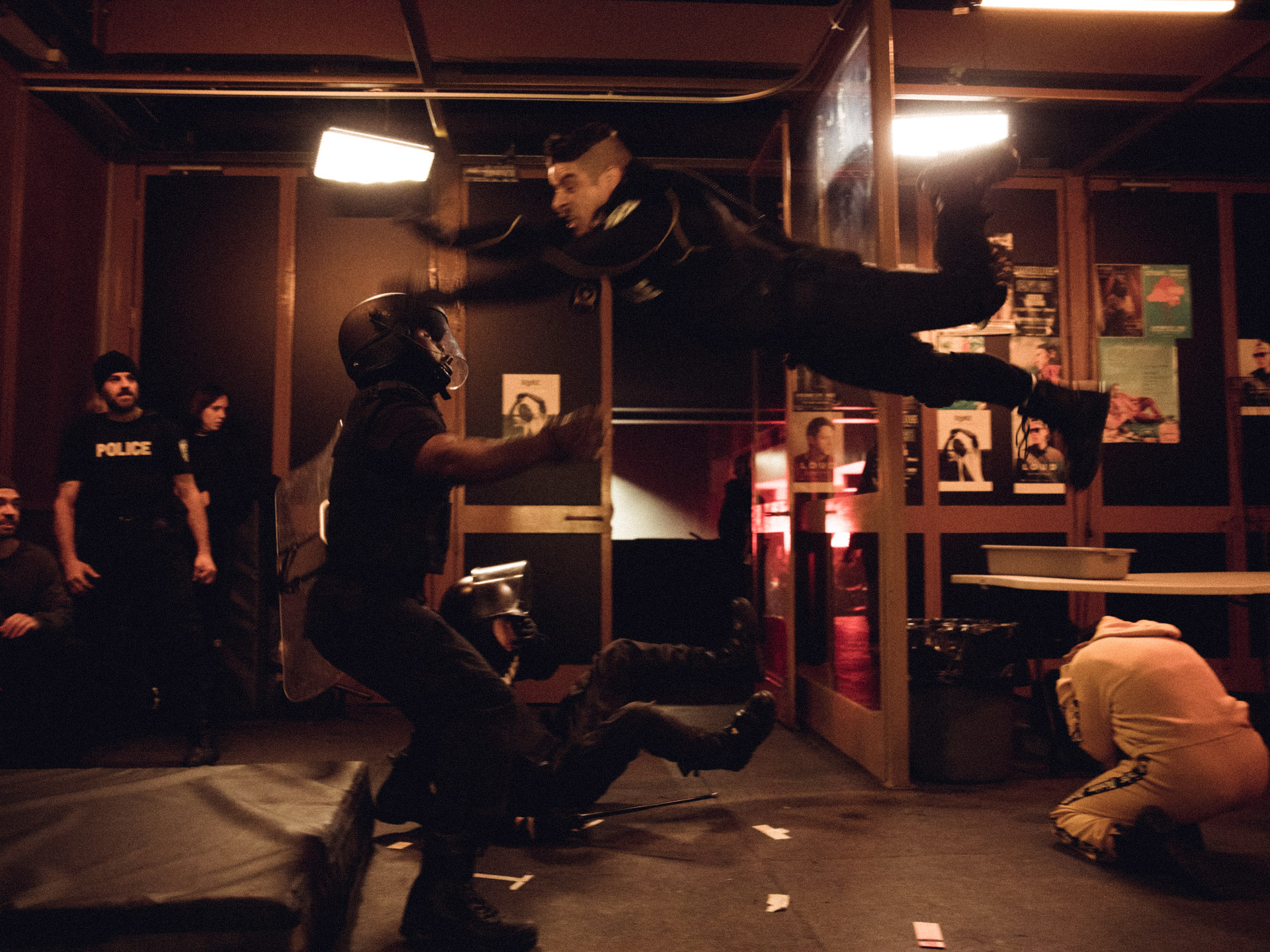 actor Hugolin Chevrette-Landesque dressed as cop jumping into the air onto another actor with safety mat behind them in behind the scenes of TV series La Loi C'est La Loi filmed by Les Gamins for TV5 Unis