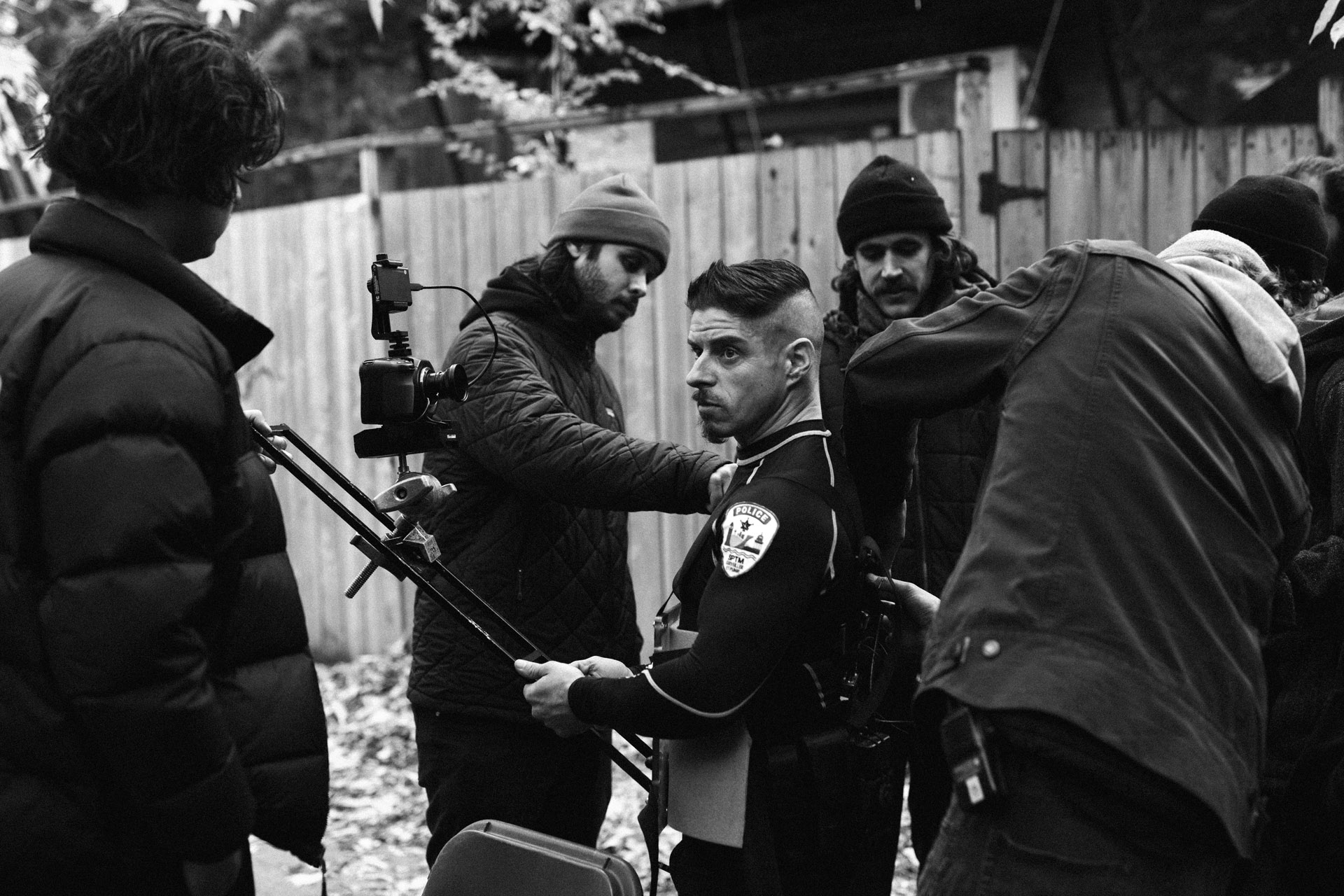 actor Hugolin Chevrette-Landesque dressed as cop getting camera harnessed on him by shooting team in behind the scenes of TV series La Loi C'est La Loi filmed by Les Gamins for TV5 Unis