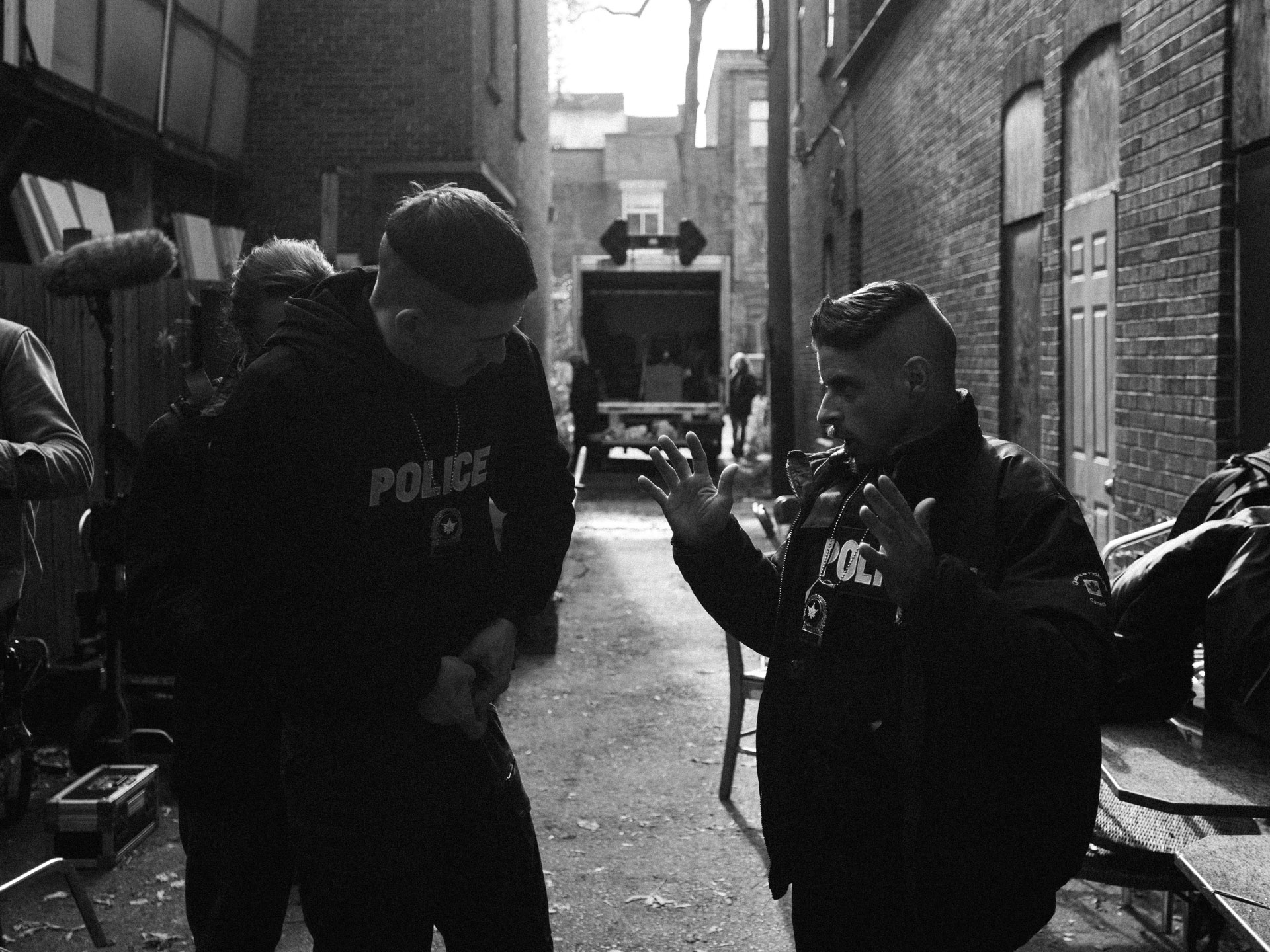 actors Hugolin Chevrette-Landesque and Emile Schneider dressed as cops talking in alley in behind the scenes for TV series La Loi C'est La Loi filmed by Les Gamins for TV5 Unis