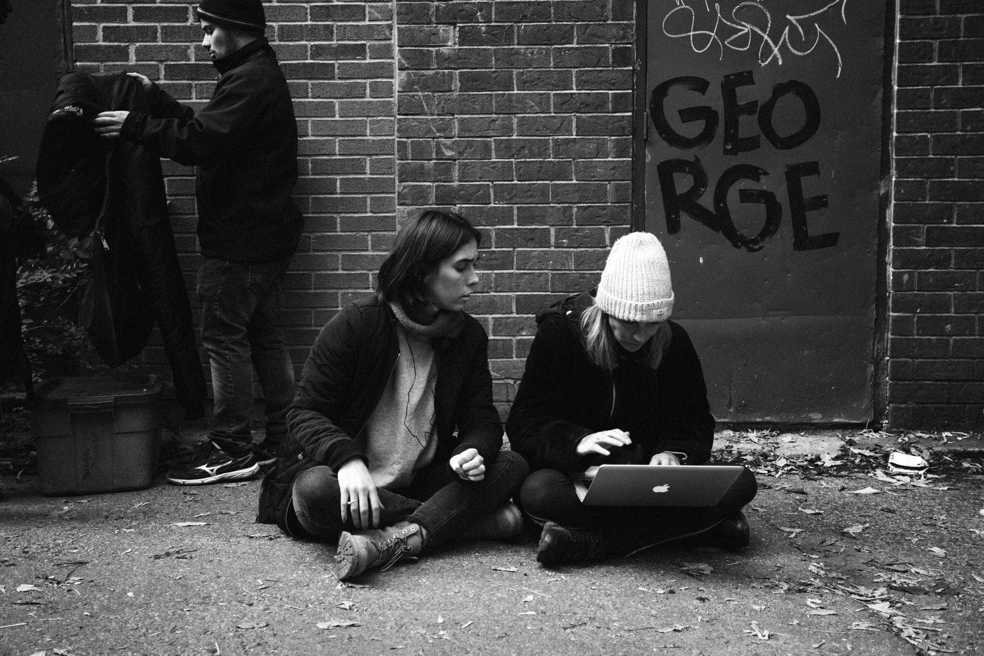 two women sitting on the ground in alley checking footage on computer in behind the scenes for TV series La Loi C'est La Loi filmed by Les Gamins for TV5 Unis