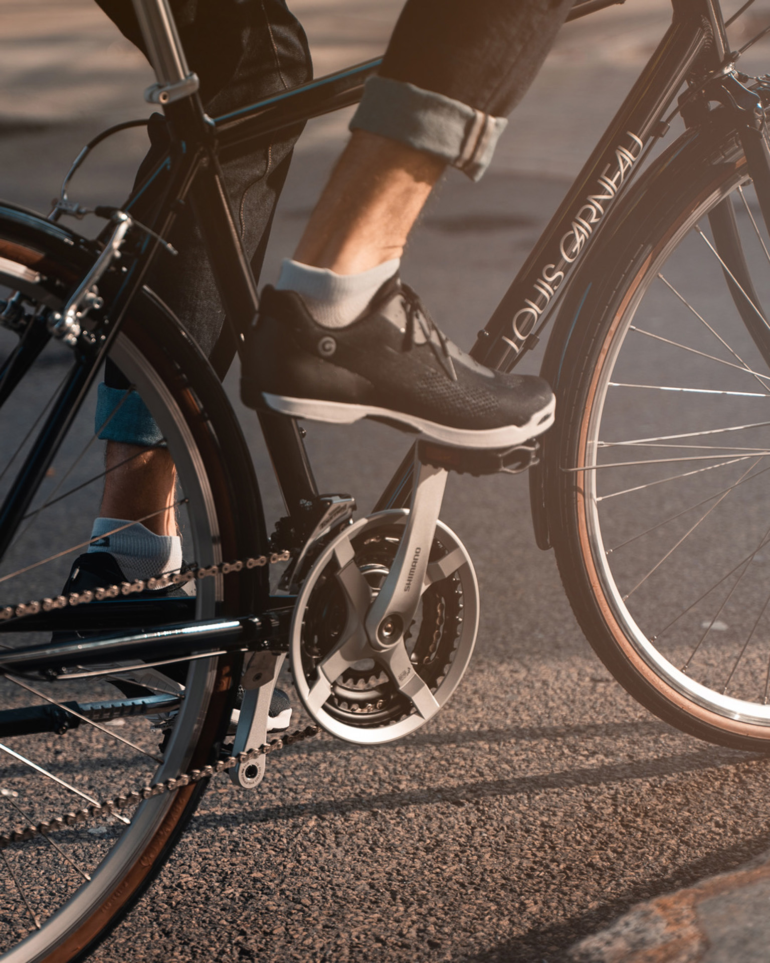 male model wearing black jeans and black shoes biking in Montreal street on black bike in the sun as Spring Summer 2020 campaign of Louis Garneau with artistic direction and styling by Studio TB