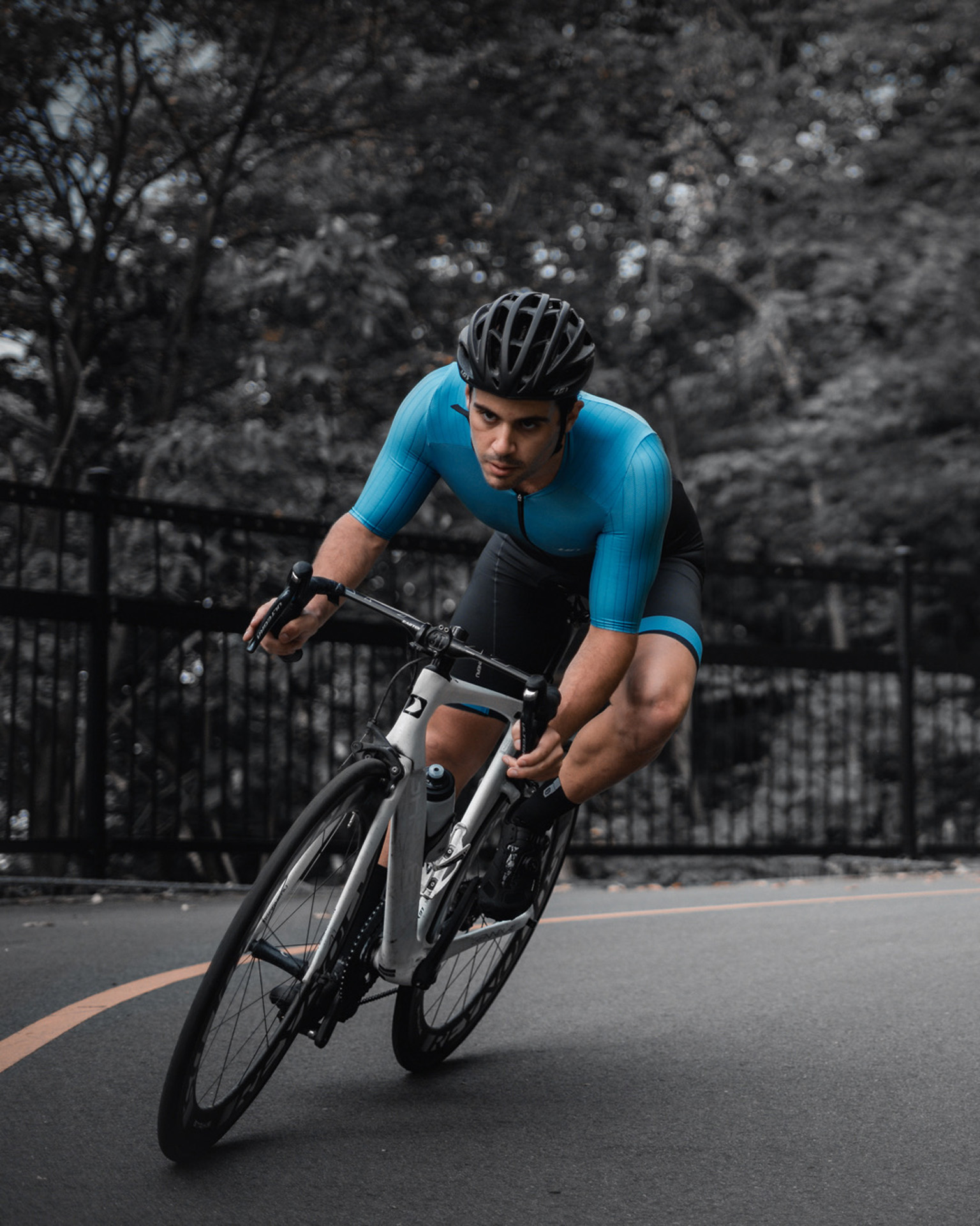 male model wearing black bike helmet and black and blue biking bodysuit biking on road on a white sports bike for Spring Summer 2020 campaign of Louis Garneau with artistic direction and styling by Studio TB