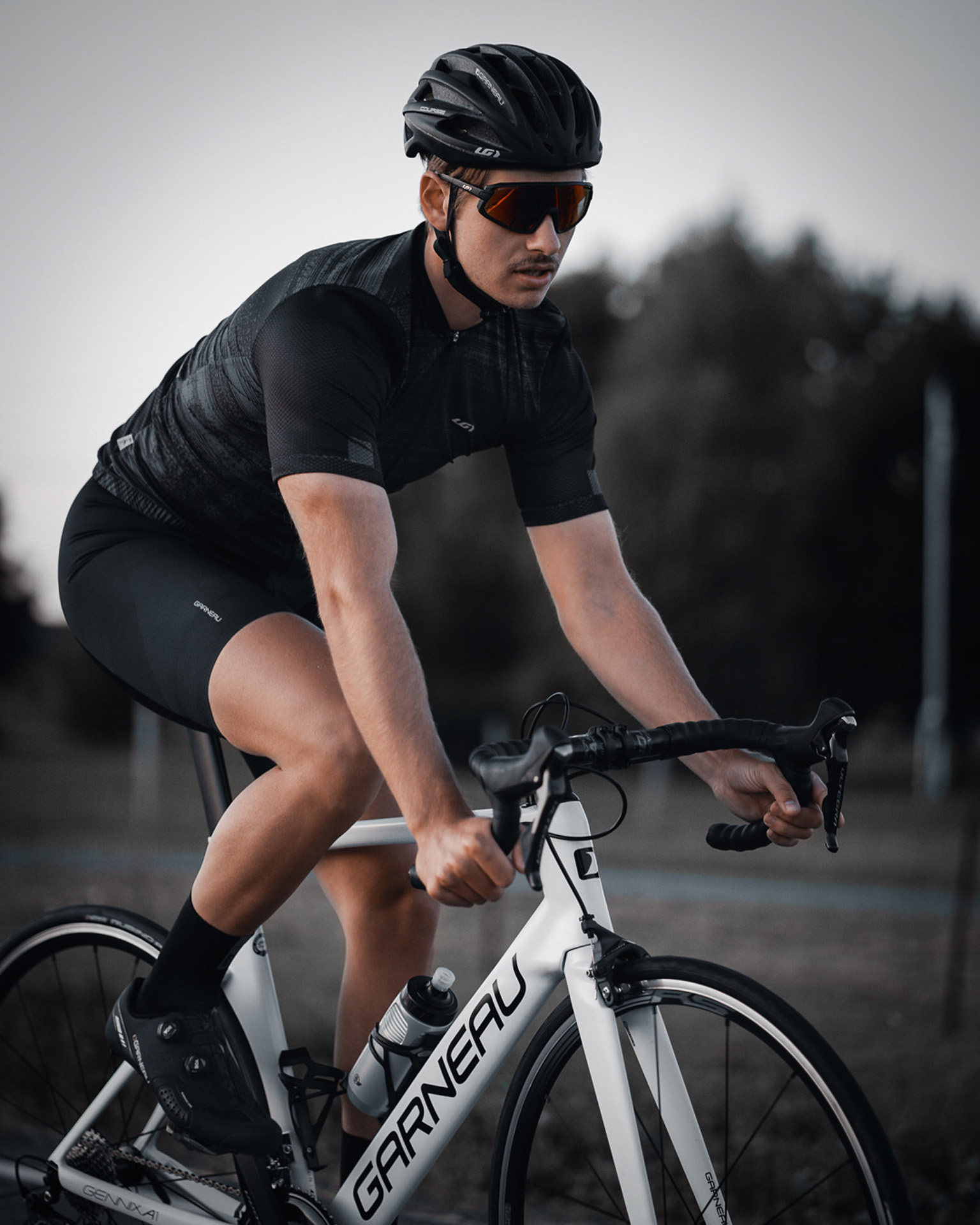 male model wearing black bike helmet and black biking bodysuit with sunglasses biking on road on a white sports bike for Spring Summer 2020 campaign of Louis Garneau with artistic direction and styling by Studio TB