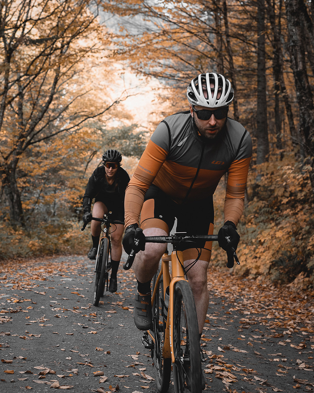 trio of long distance bikers biking on dirt road one behind the other with mountains covered in orange colored trees in the background for Spring Summer 2020 campaign of Louis Garneau with artistic direction and styling by Studio TB