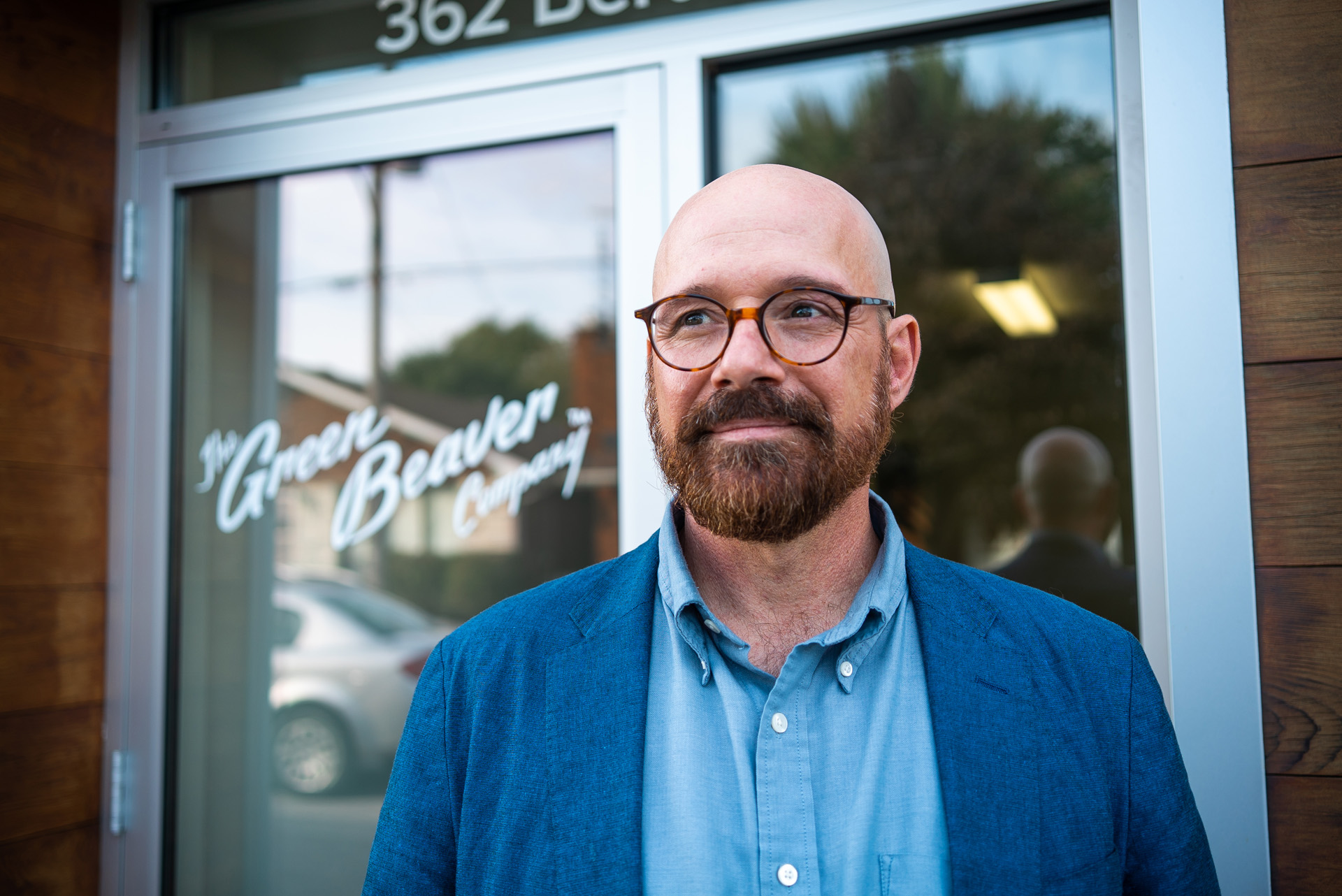 bald man in front of Green Beaver Company wearing blue blazer glasses and beard by Bruno Florin for BDC Beyond Business with Cossette