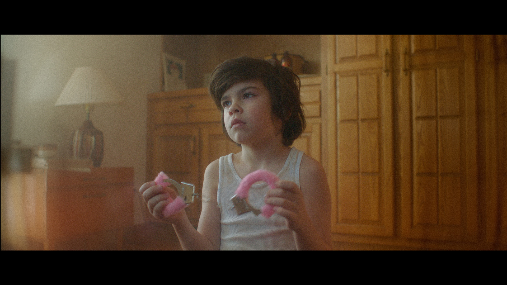 kid looking at TV holding fuzzy pink handcuffs in TV series La Loi C'est La Loi filmed by Les Gamins