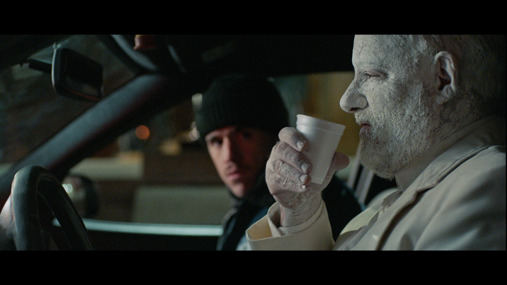 actor Emile Schneider posing as cop in a car sitting next to man completely painted white drinking a cup of water for TV series La Loi C'est La Loi filmed by Les Gamins for TV5 Unis