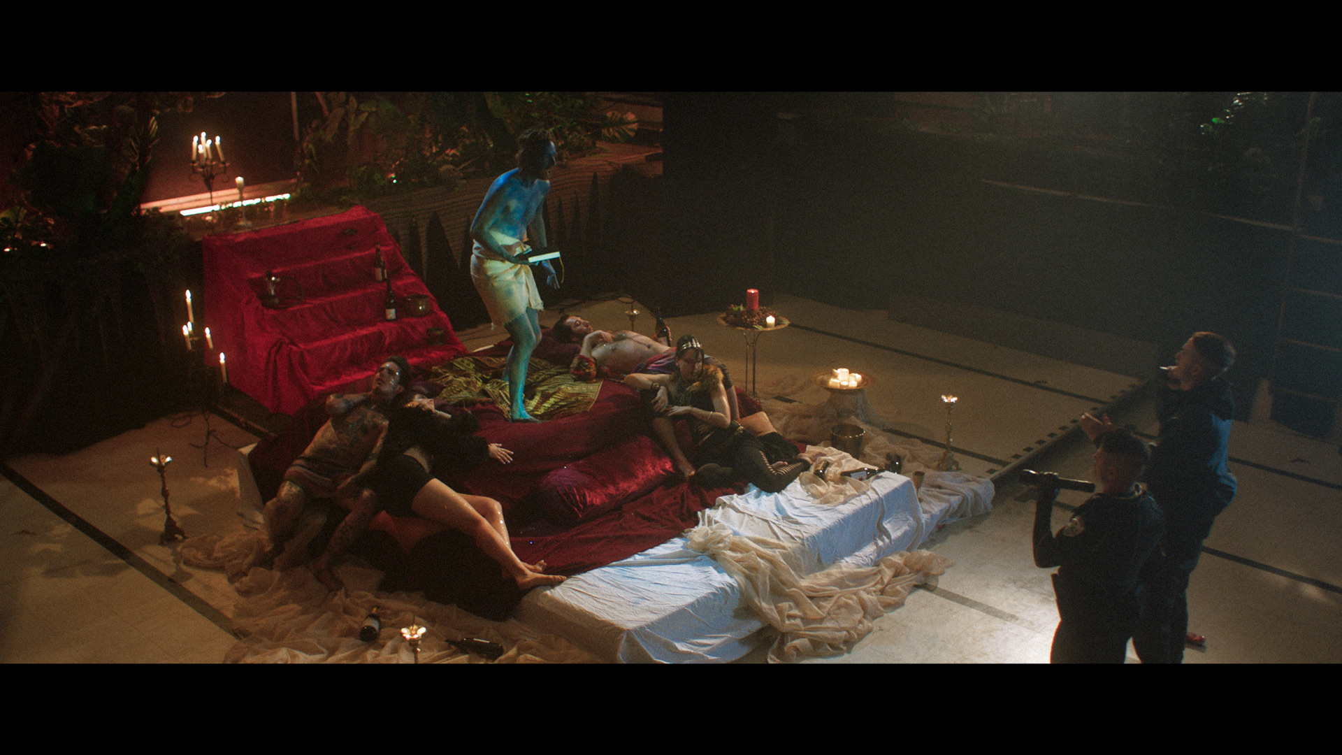 actor completely painted in blue from head to toe playing a guru standing on stage-bed surrounded by people laying blissfully at his feet while guru screams at police officers played by Hugolin Chevrette-Landesque and Emile Schneider for TV series La Loi C'est La Loi filmed by Les Gamins for TV5 Unis