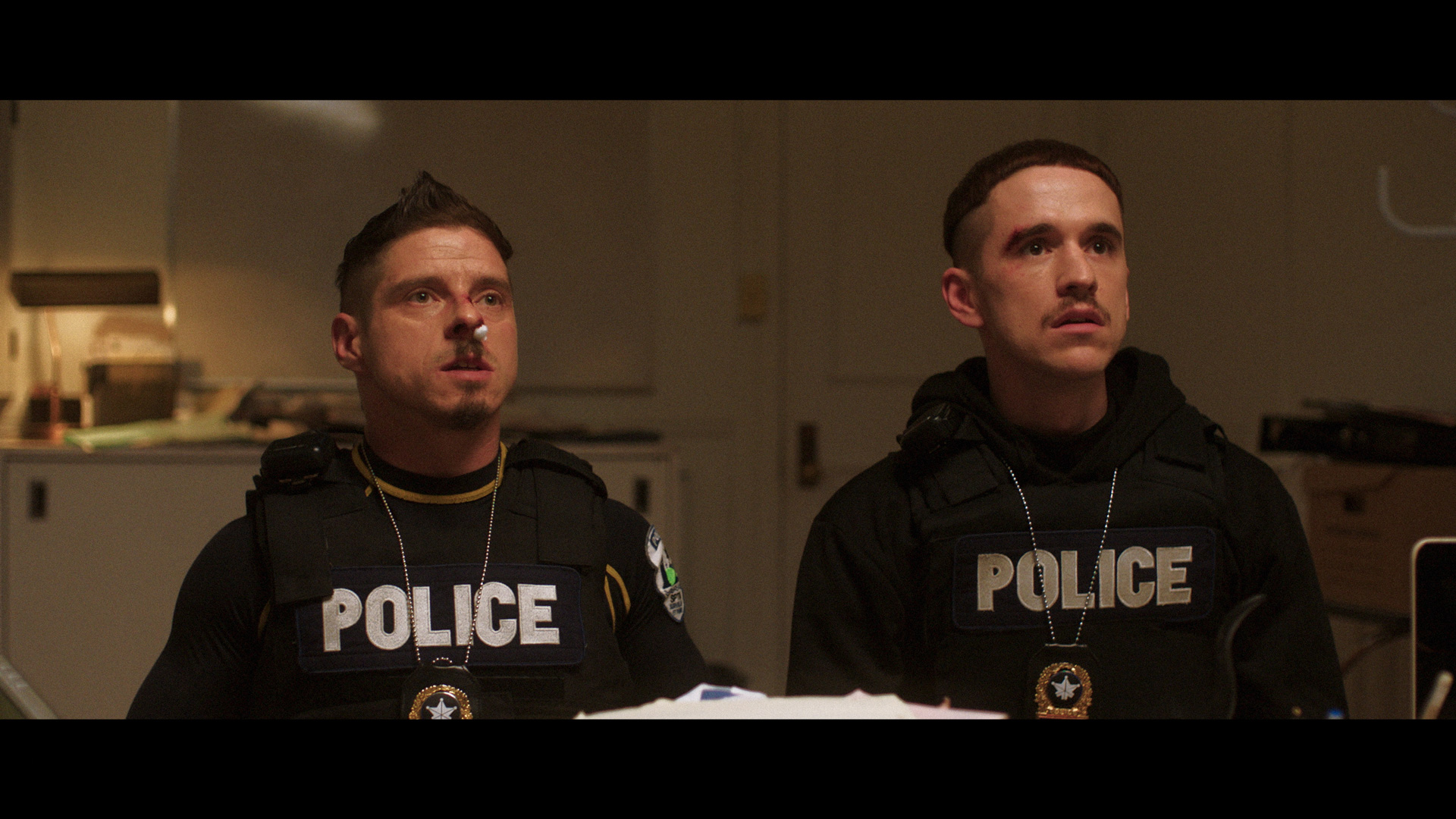 actors Hugolin Chevrette-Landesque and Emile Schneider posing as cops looking beaten up with noses bleeding sitting in their chief's office for TV series La Loi C'est La Loi filmed by Les Gamins for TV5 Unis
