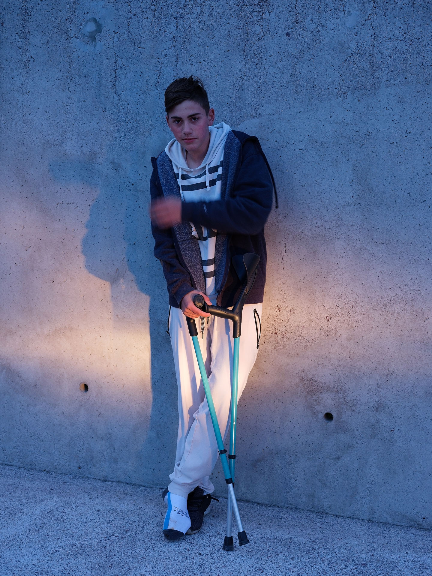 young boy posing against wall using blue crutches by Guillaume Simoneau in Saint-Pierre-et-Miquelon for M le mag Le Monde