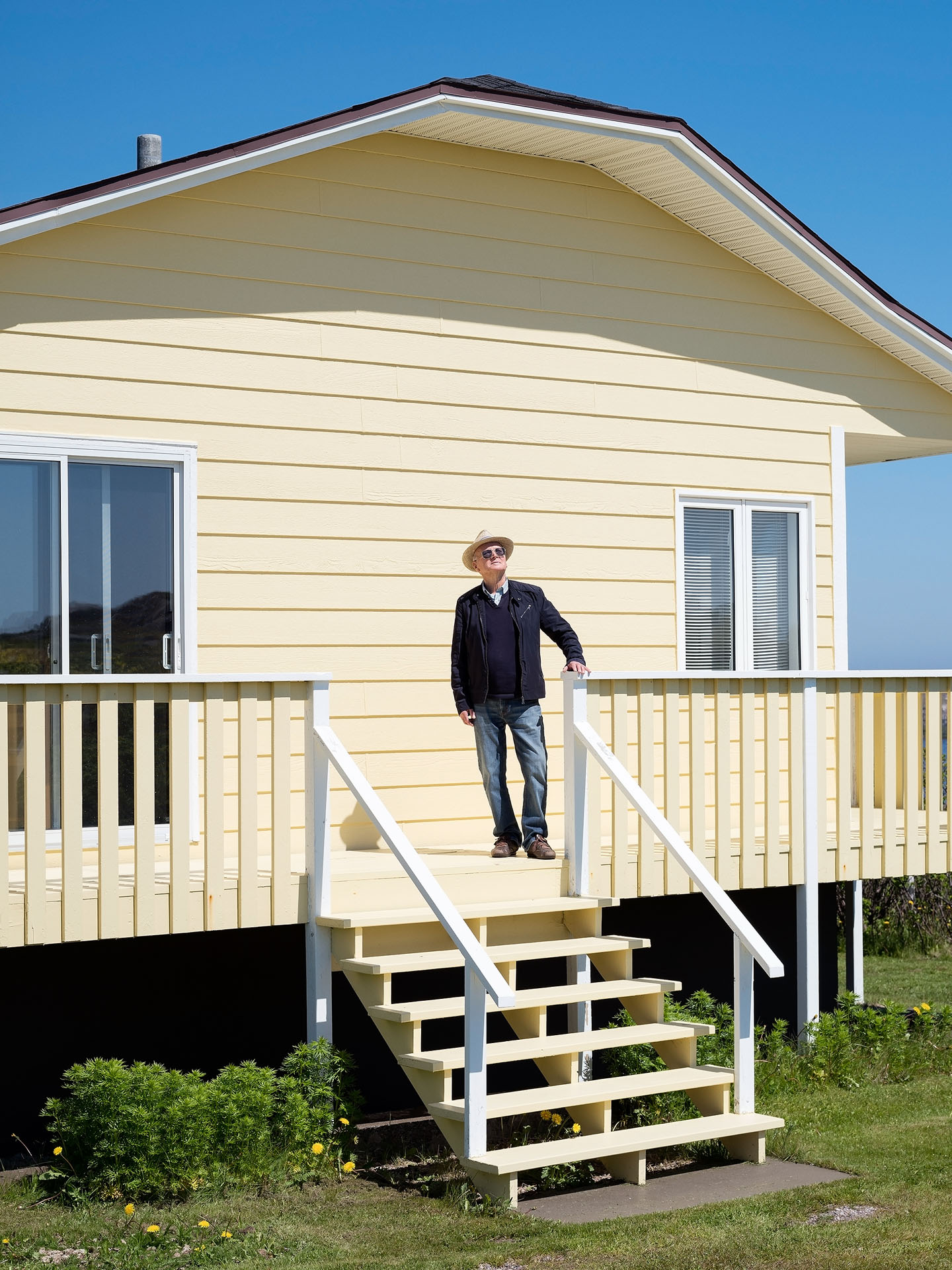 french style seaside yellow house with old man in the front porch looking at the sky by Guillaume Simoneau in Saint-Pierre-et-Miquelon for M le mag Le Monde