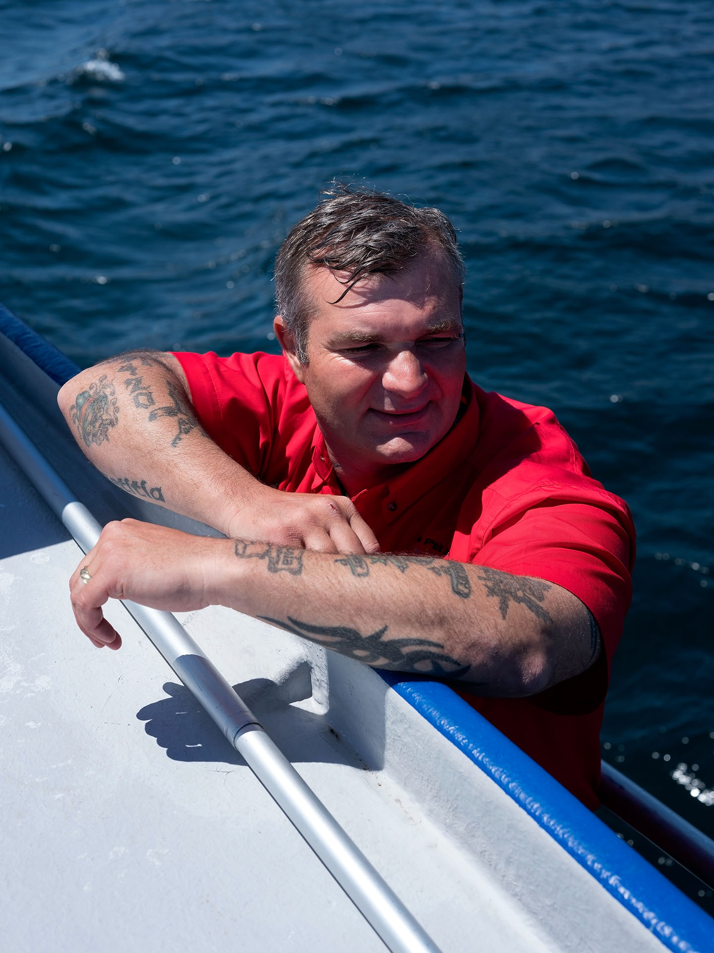 man with red shirt in the water leaning against side of boat by Guillaume Simoneau in Saint-Pierre-et-Miquelon for M le mag Le Monde