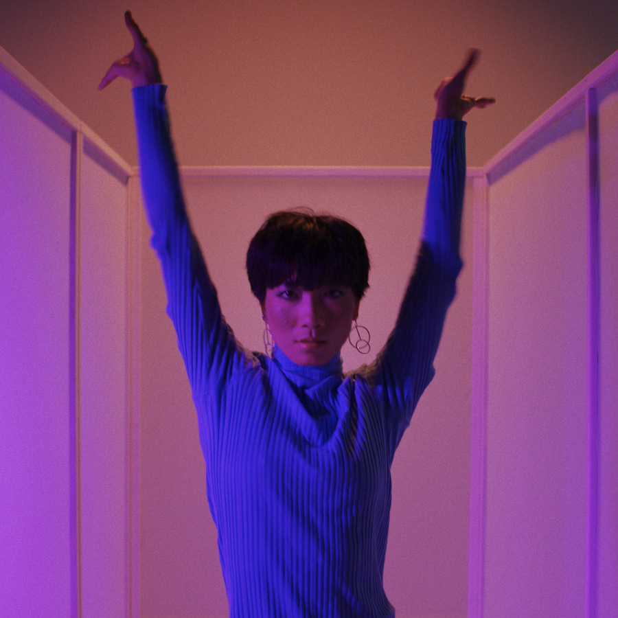 asian dancer arms in the air looking at camera in blue lighting on pink background for Fabrikate by Simon Duhamel