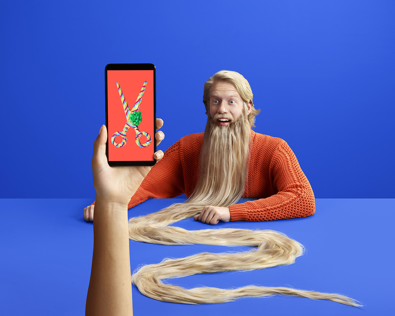 surrealist shot of a man with a very long beard and a hand holding a mobile phone displaying scissors by Simon Duhamel for FIzz