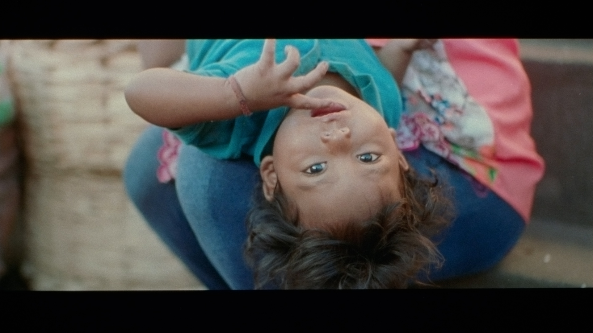 young kid laying in a woman's arms looking at camera upside down with fingers in their mouth singer Karim Ouellet music video of La Mer A Boire filmed by Les Gamins