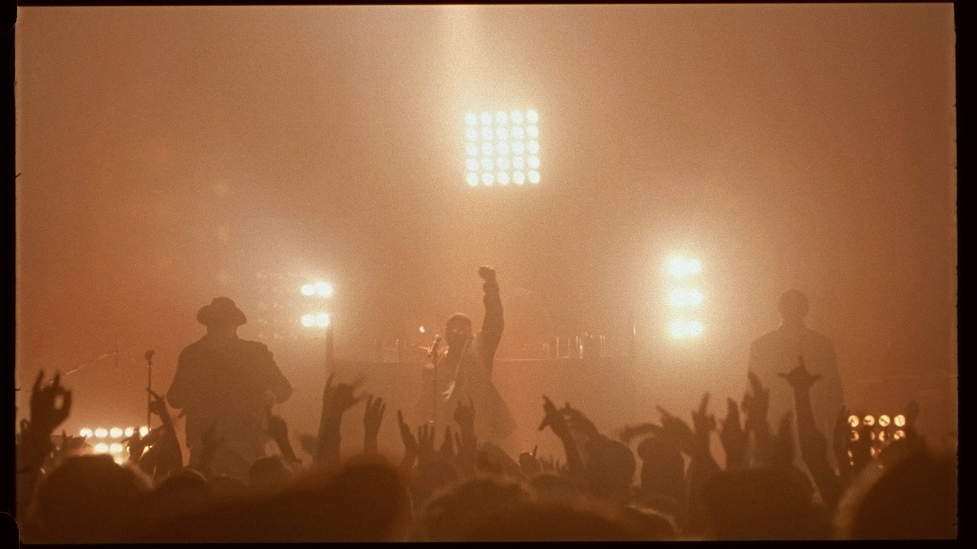 singer Brown on stage with his fist raised up in the air in front of crowd bathed in soft orange light for L'Osstidfilm documentary filmed by Vincent Ruel-Cote from Les Gamins about L'Osstidtour