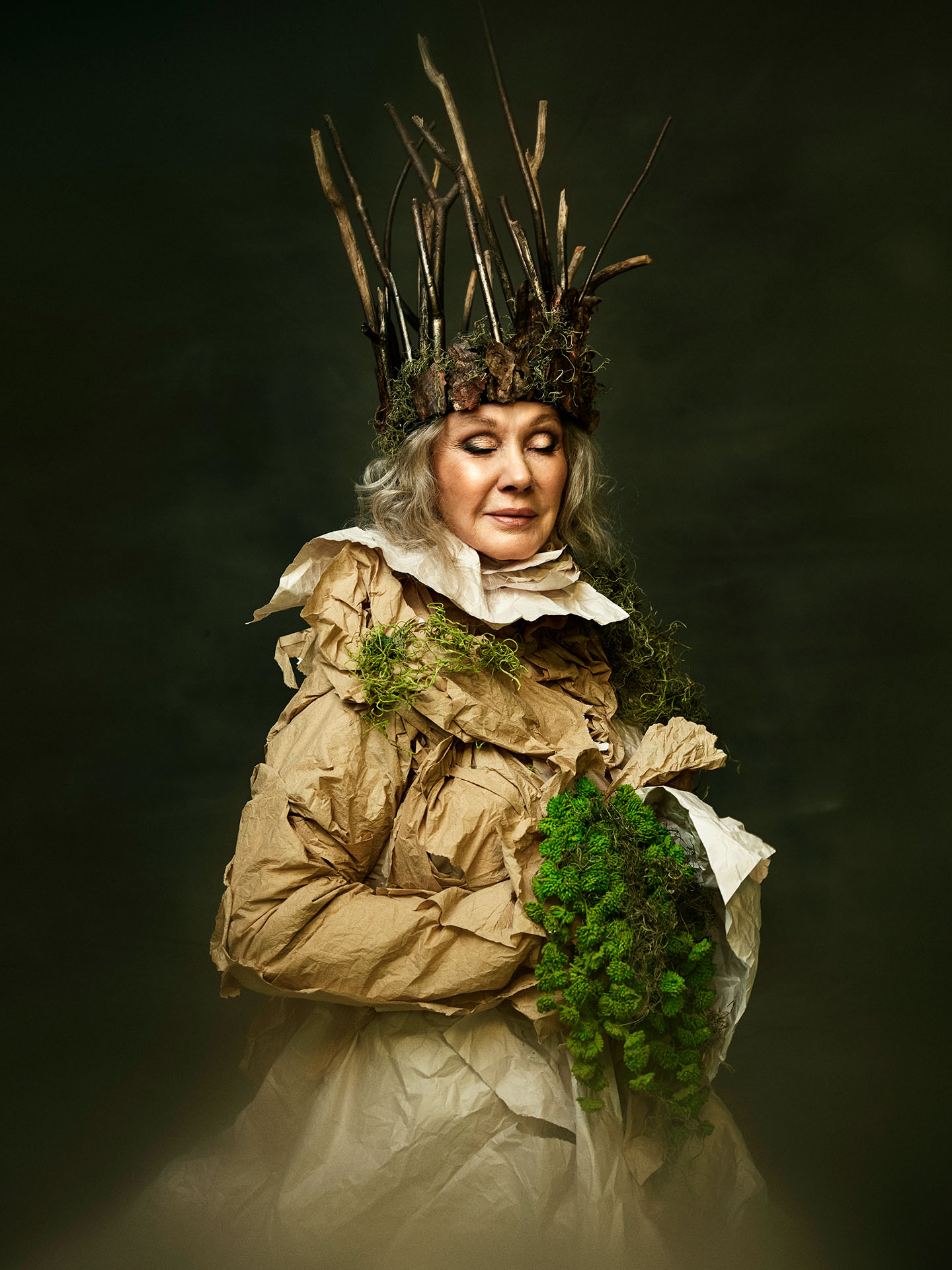 portrait of Diane Dufresne dressed in long brown paper dress with wood branches crown and moss bouquet by Jocelyn Michel for Voir